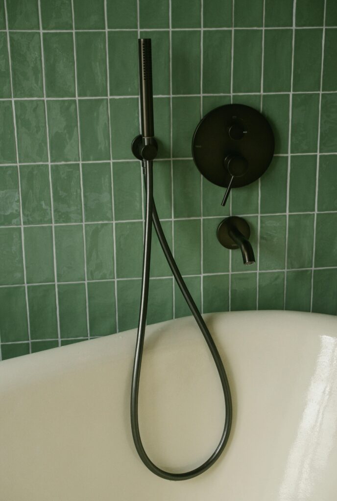 pexels-photo-32662272-32662272 Modern bathroom featuring green tiles, a clean bathtub, and sleek black fixtures.