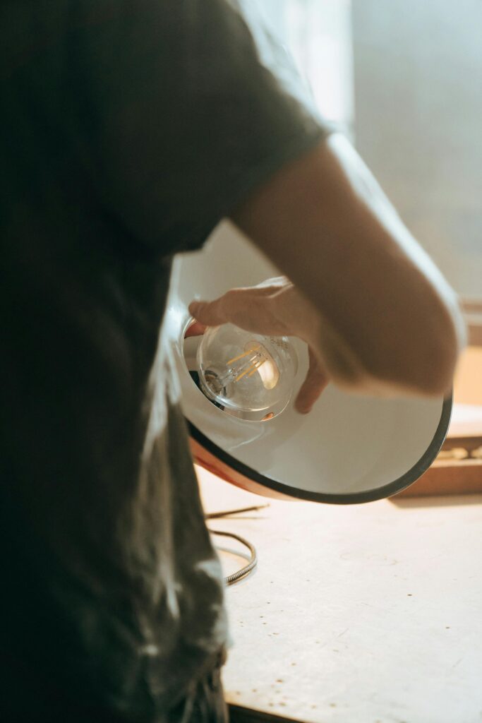 pexels-photo-5090642-5090642 Person adjusting a vintage lightbulb inside a repair workshop setting.