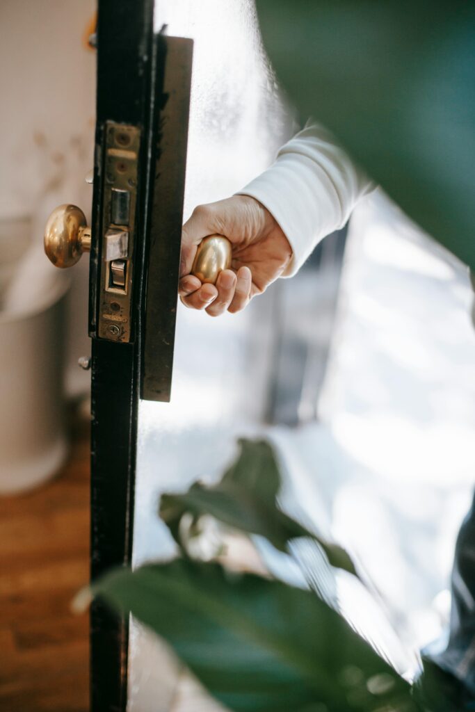 pexels-photo-5825395-5825395 Close-up of a hand opening a door with a brass handle leading to a bright interior.