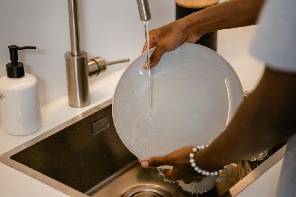 pexels-photo-7641231-7641231 A close-up view of a person washing a plate in a modern kitchen sink with water running from the faucet.