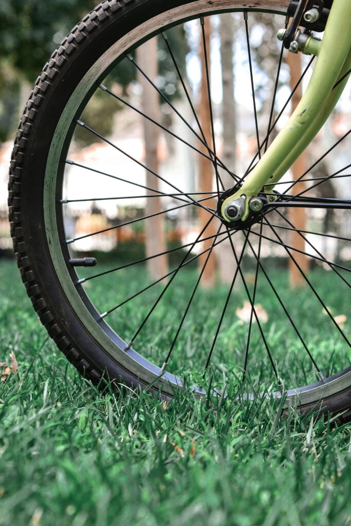 Close-up of a bicycle wheel resting on green grass outdoors. Ideal for adventure themes.