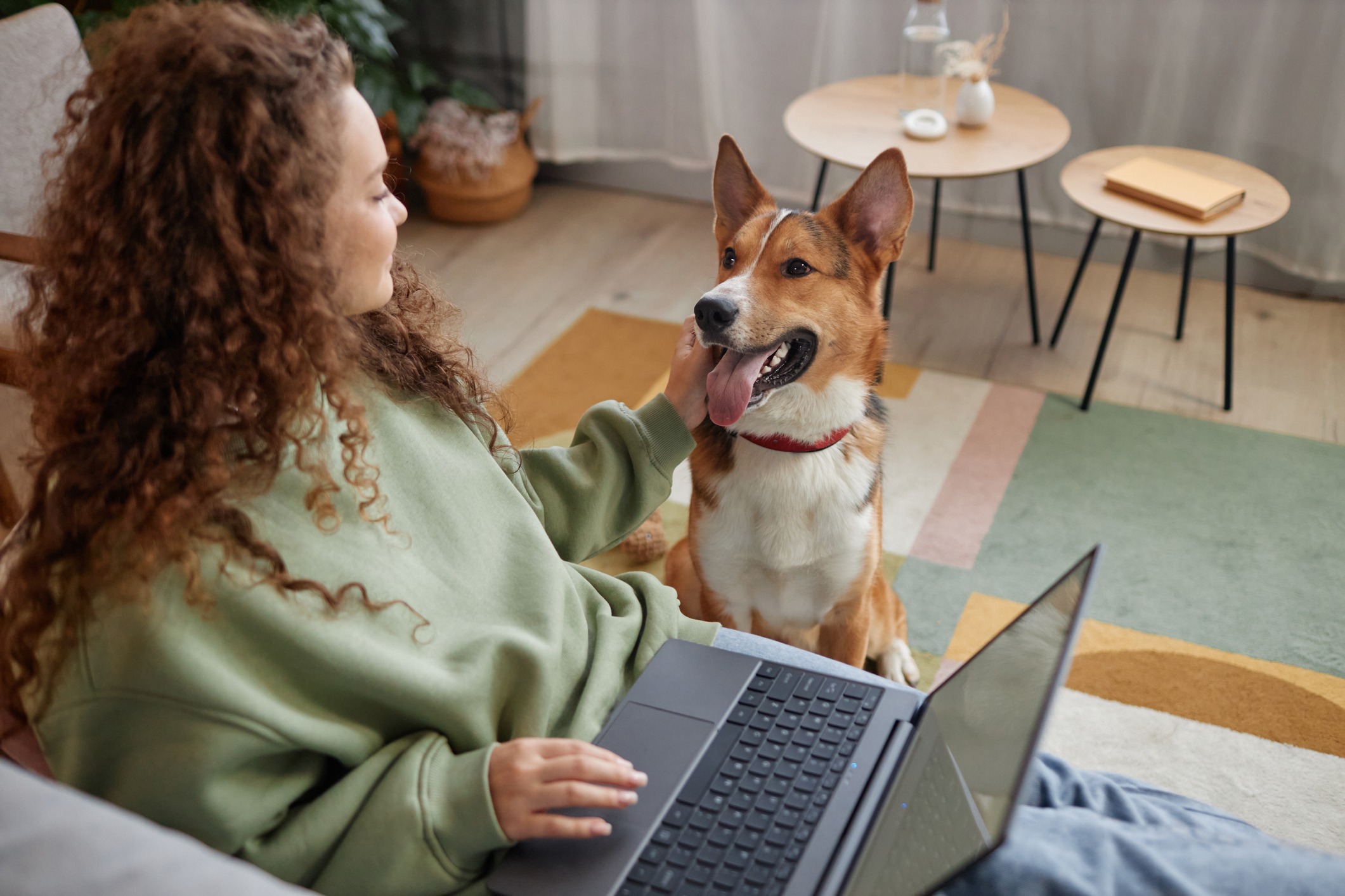 Young barefoot African American female with cup of hot drink standing on floor with dog at home